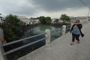 Una mujer se tapa la nariz y apura el paso al cruzar por un puente sobre el estero Salado, en el suburbio porteño.