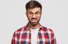 photo-of-irritated-unshaven-man-looks-angrily-clenches-teeth-and-raises-eyebrows-being-annoyed-with-much-duties-on-work-dressed-in-checkered-shirt-stands-against-white-wall