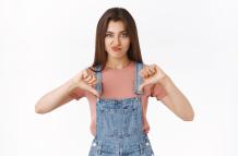 disappointed-skeptical-arrogant-attractive-woman-in-overalls-t-shirt-smirking-unsatisfied-showing-thumbs-down-and-frowning-in-disagreement-express-dislike-judge-something-awful