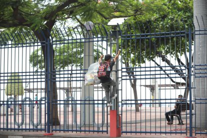 Un comerciante trepa las rejas, evitando a los guardias que no lo dejan pasar por las puertas.
