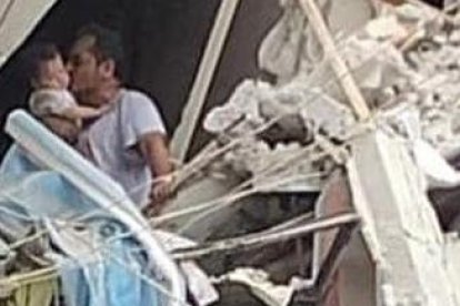 Escenario. Es un hombre, aferrádose a lo que queda de una pared y con los pies sobre una casa a punto de derrumbarse, pero quien se muestra feliz de que la vida que carga en sus brazos esté intacta.