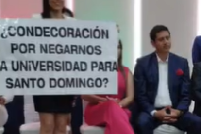 Liliana Silva sostiene un cartel de rechazo, mientras Viviana Veloz (der.) es reconocida en Santo Domingo.