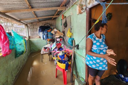 Mujer observa con preocupación la entrada de su vivienda inundada en Esmeraldas, mientras intenta proteger sus pertenencias del agua acumulada en el interior.