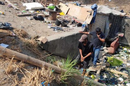 Miguel y Rolando caminan por un puente improvisado para entrar y salir de la covacha.