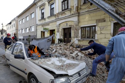 Personas y soldados limpian los escombros junto a automóviles y edificios dañados por un terremoto en Petrinja, Croacia.