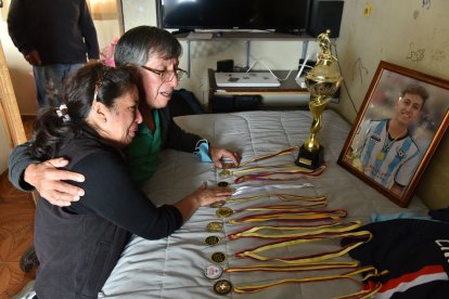 La madre y el abuelo del joven en el dormitorio donde él dormía. Muestran sus medallas.