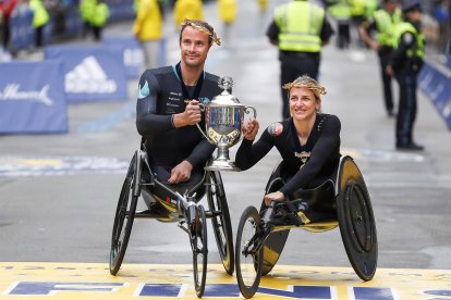 Marcel Hug (izq.) Y Manuela Schar de Suiza posan en la línea de meta con el trofeo después de ganar respectivamente las carreras en silla de ruedas masculina y femenina del 125 ° Maratón de Boston .