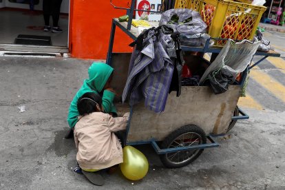 Niños acompañan a sus padres a trabajar con una carreta de productos vegetales en una calle de Quito.