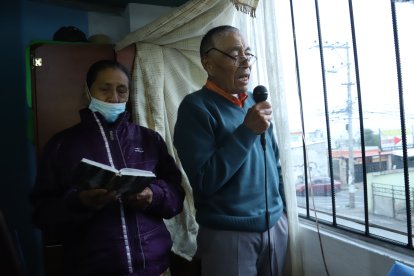 Por una ventana, el hombre, acompañado de su esposa, habla para los vecinos y recita varios versículos de la Biblia.