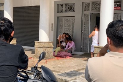 Familiares de la víctima lloran junto a su cadáver, al que han cubierto con sábanas, en la entrada de su casa.