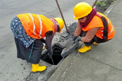 Dos mujeres de una de las microempresas realizan labores de limpieza en los drenajes de una de las vías de Tungurahua.