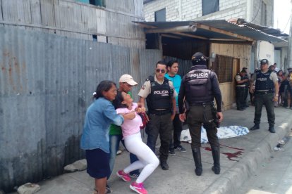La mujer es contenida por un pariente. Ambos están cerca del cadáver.