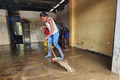 Varias personas retiran el agua lodo que quedó dentro de su vivienda, con una escobas que compraron.