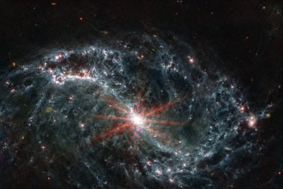 Imagen real tomada por el telescopiop espacial James Webb de una galaxia espiral gris con forma de telaraña sobre un fondo negro.