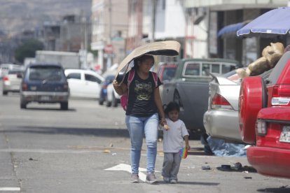 Una mujer usó un cartón para taparse del sol mientras caminaba con una niña.