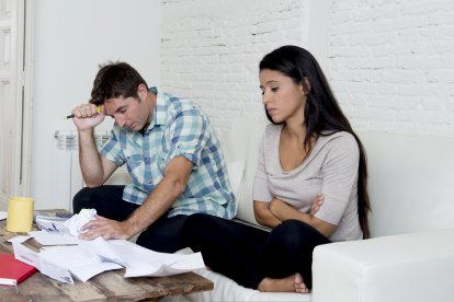 young sad couple at home living room couch calculating monthly expenses worried in stress with bank papers and documents in paying taxes , mortgage debt and cost of living concept