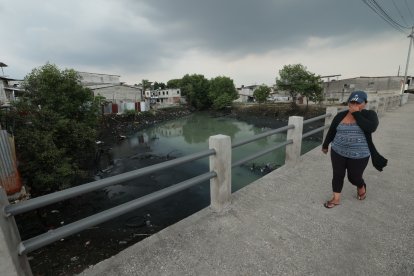 Una mujer se tapa la nariz y apura el paso al cruzar por un puente sobre el estero Salado, en el suburbio porteño.