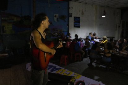 Artista toca la guitarra sobre una tarima oscura, por falta de luz.