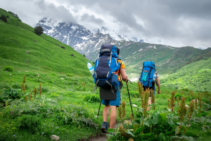 Dos turistas subiendo una montaña como excursionistas, disfrutando del paisaje mientras avanzan.