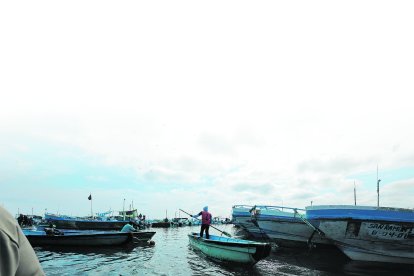 Un hombre se abre paso entre las embarcaciones pesqueras. En el puerto no funciona el retén naval.