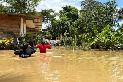 Dos personas avanzan con dificultad entre aguas turbias que cubren gran parte de la comunidad de San Gregorio, mientras viviendas y cultivos permanecen bajo el nivel de la inundación.
