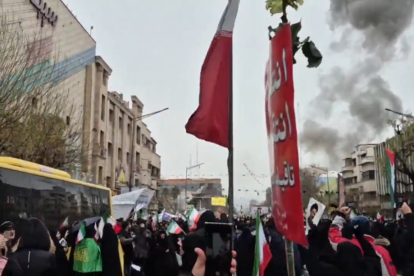 Manifestantes marchan en Teherán mientras humo de una explosión se observa a lo lejos