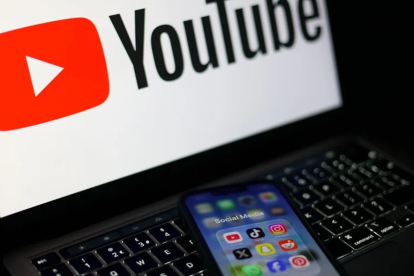 Pantalla con el logo de YouTube, propiedad de Alphabet, y un móvil con aplicaciones de redes sociales como Instagram y Facebook