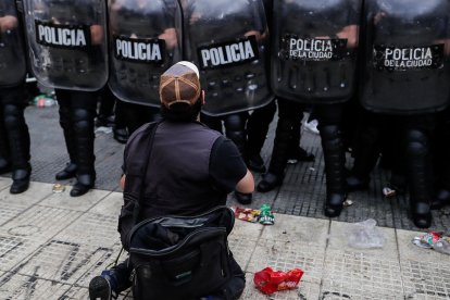 Una persona se arrodilla delante de la policía durante la espera para poder ingresar al velatorio.