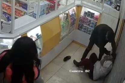 El delincuente le pone el arma en la cabeza, mientras su cómplice roba el dinero. Luego la tira al piso y le amarra las manos.