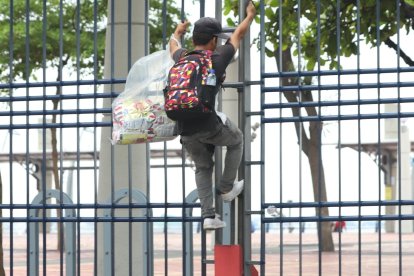 Un comerciante trepa las rejas, evitando a los guardias que no lo dejan pasar por las puertas.