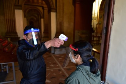 Un encargado toma la temperatura de los fieles antes de entrar a las iglesias.