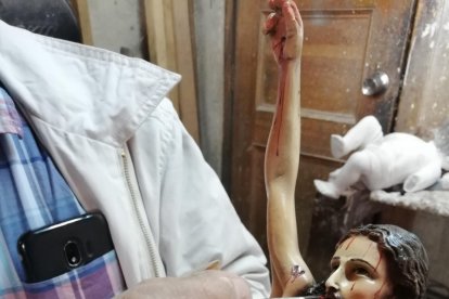Édgar Guerrero reparan la pintura a un Crucifijo.