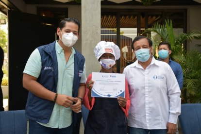 Una de las participantes del taller de Gastronomía básica recibe su certificado. La acaompañan funcionarios del Mies.