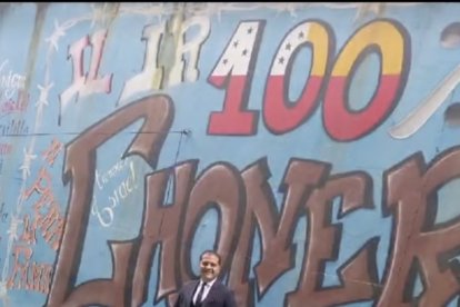 Posa delante de un grafiti que hace alusión a la organización criminal.