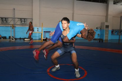 Patrick ya no entrena con botellones ni taque de gas. En la gráfica, levanta a su compañero Isaac para realizar sentadillas con peso.