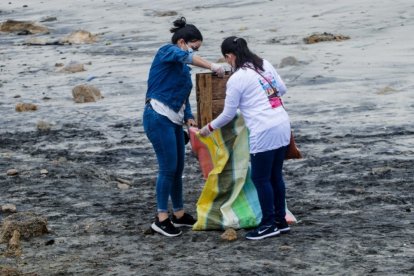 Dos mujeres ponen en sacos los restos de un enser doméstico. Parece que la playa aguanta todo.