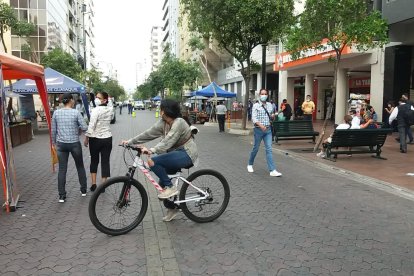 Una ciclista circula por la calzada mientras peatones pasean descomplicados.