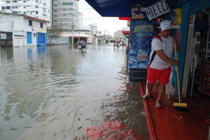 El propietario de un negocio internta evacuar el agua que entró a su local.