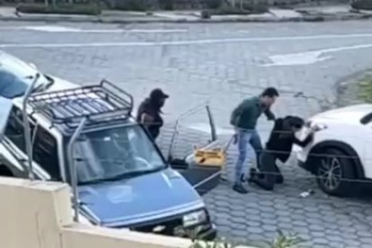 Una persona ayuda a la joven, arrimada al carro blanco. Detrás está el atacante.