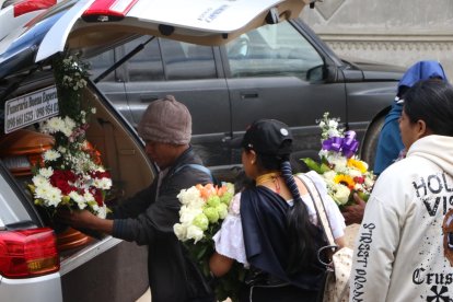 Los allegados colocan arreglos florales en la carroza fúnebre.