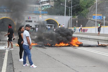 Personas observan una vía bloqueada por neumáticos en Caracas.
