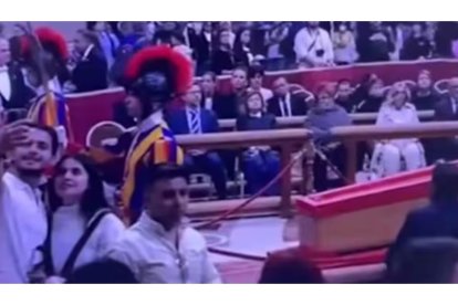 Una pareja tomándose fotos mientras sonríen frente al féretro del papa Francisco.