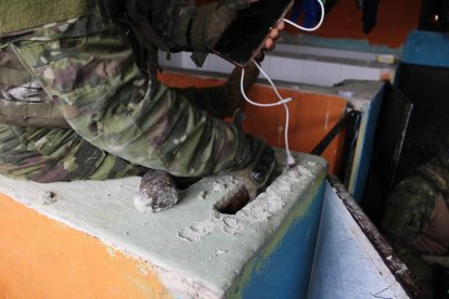 Un militar saca un celular y un cargador de un hueco realizado en la pared de una de las celdas.