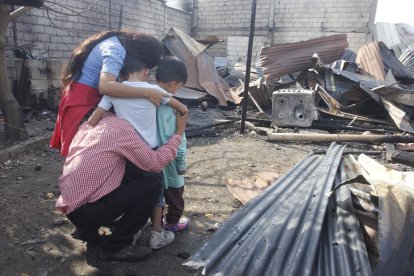 Vicente y su esposa, Nicolle, abrazan a sus hijos mientras contemplan con desconsuelo lo que quedó de su hogar.