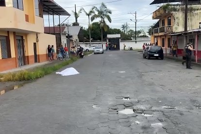 El cuerpo de la docente Diana Alcívar yace cubierto en la calle, mientras policías acordonan el área y al fondo se observa el Colegio Técnico Nueva Concordia.”