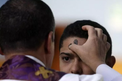 Un sacerdote impone la ceniza a un joven en la misa del Miércoles de Ceniza.