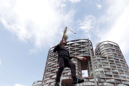 Equilibrio. Un artista urbano en monociclo mantiene el equilibrio mientras realiza malabares en plena avenida, con la ciudad elevándose imponente a sus espaldas.