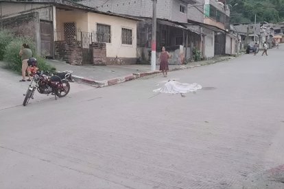 Vecinos del barrio Santas Vainas observan consternados la escena donde un joven fue asesinado a tiros; su cuerpo quedó cubierto con una sábana en medio de la calle.