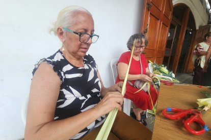 Dos mujeres de la parroquia Nuestra Señora de Montebello trabajan con paciencia y destreza las hojas de palma, transformándolas en ramos artesanales