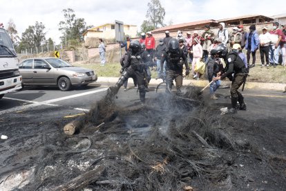 Agentes policiales intervienen para retirar un bloqueo de la vía, mientras manifestantes observan a un costado tras la quema de neumáticos y troncos durante una jornada de protesta.